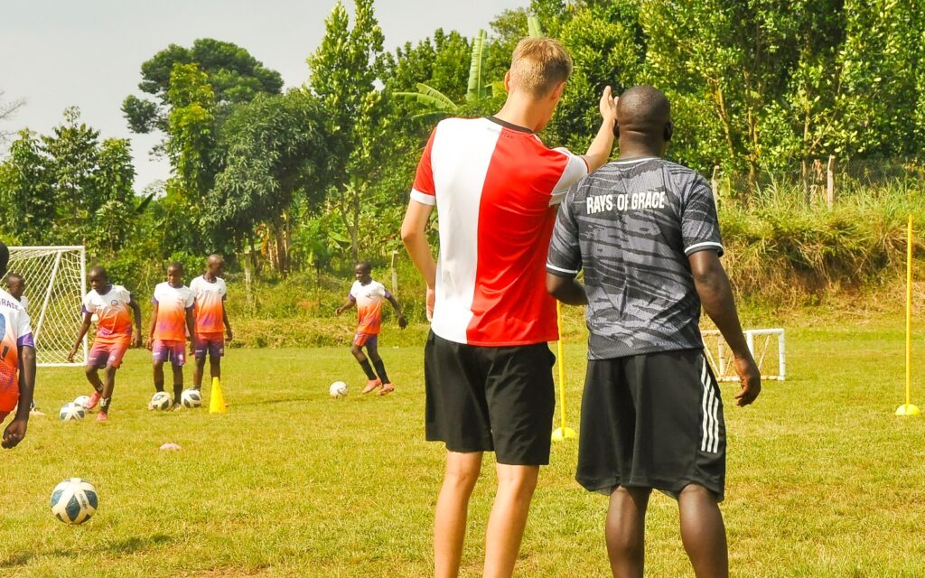 Leon Kampman begeleidt een voetbalcoach langs het veld en geeft praktische aanwijzingen tijdens een training.
